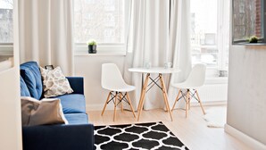 Een moderne woonkamer met een blauwe bank, twee witte stoelen, een kleine tafel en een raam met gordijnen.