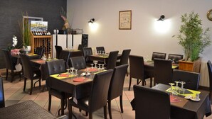 A dining area with multiple tables set for guests, featuring black chairs and a wine rack. - L'Hôtel du Port (Port-la-Nouvelle)