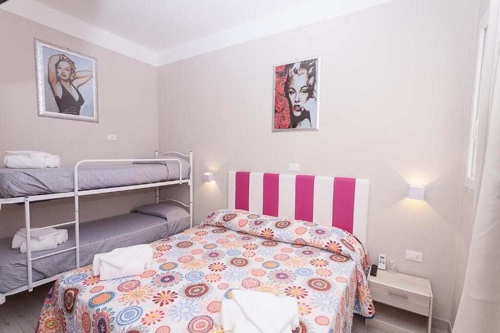 Ein Zimmer mit Etagenbetten, einem Bett mit farbig gemustertem Bettbezug und zwei Wandleuchten.