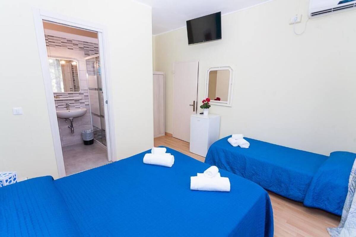 Une chambre d’hôtel avec deux lits, une télévision, un miroir et une salle de bain visible à travers une porte ouverte.