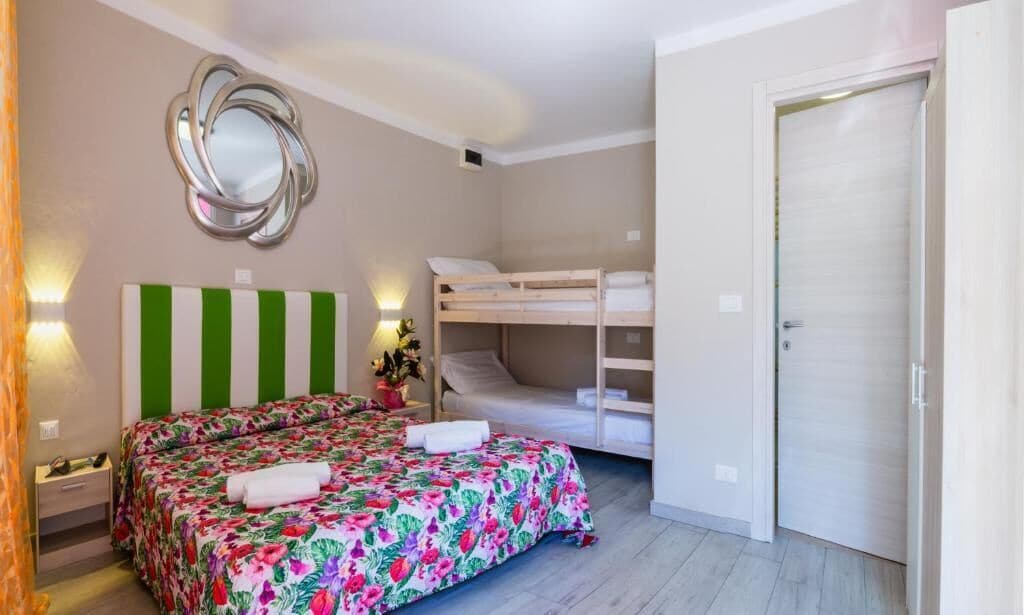 A bedroom with a bunk bed, a bed with a floral bedspread, a mirror, and a door.