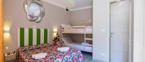 A bedroom with a bunk bed, a bed with a floral bedspread, a mirror, and a door.