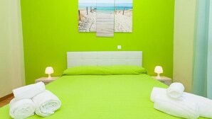 Habitación de hotel con una pared verde brillante, una cama con cabecera blanca, dos lámparas de noche y una obra de arte con motivos playeros sobre la cama.