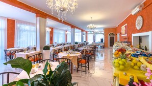 Un comedor amplio con varias mesas y sillas, un candelabro y un bufé con diferentes alimentos.