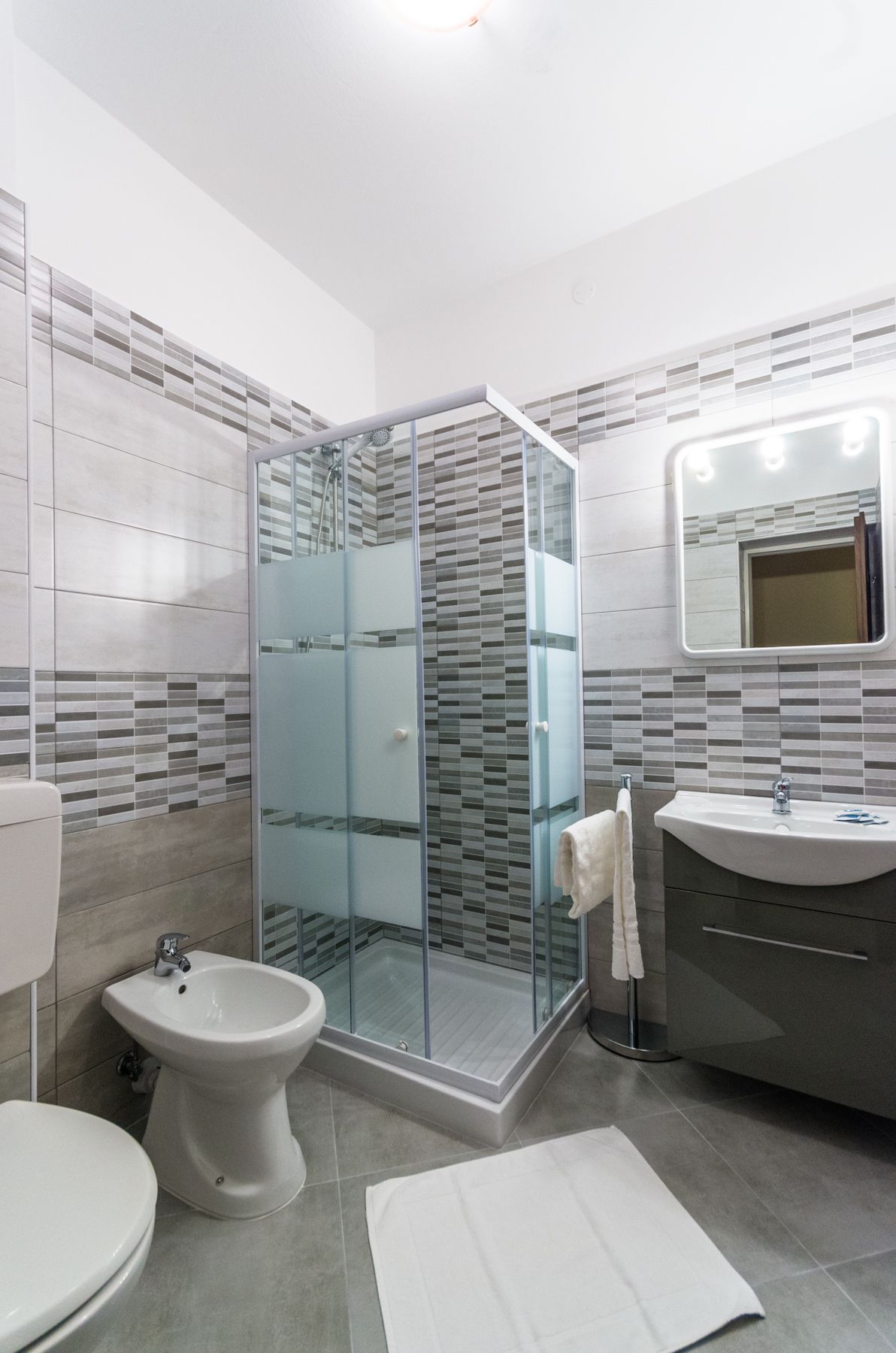 A modern bathroom with a glass-enclosed shower, a bidet, a sink, and a mirror with lights.