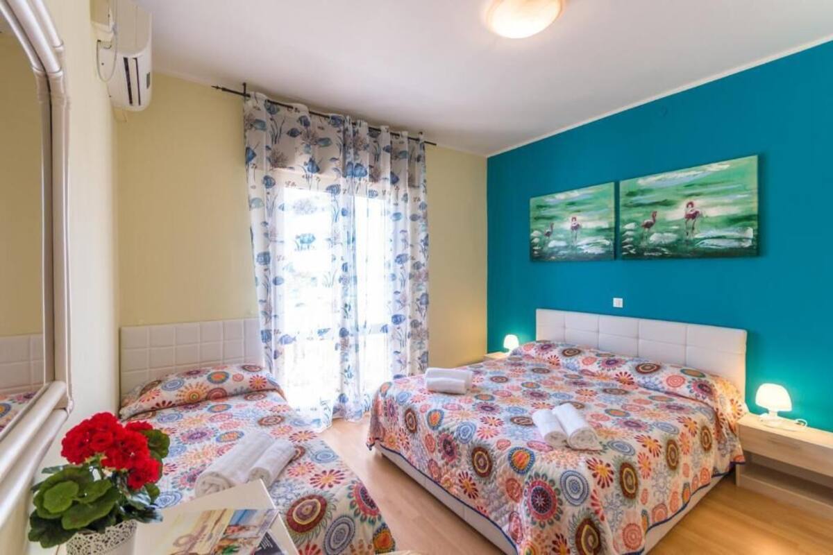 Une chambre avec deux lits, des rideaux à motifs floraux, un mur d’accent de couleur turquoise et un tableau représentant des flamants roses.