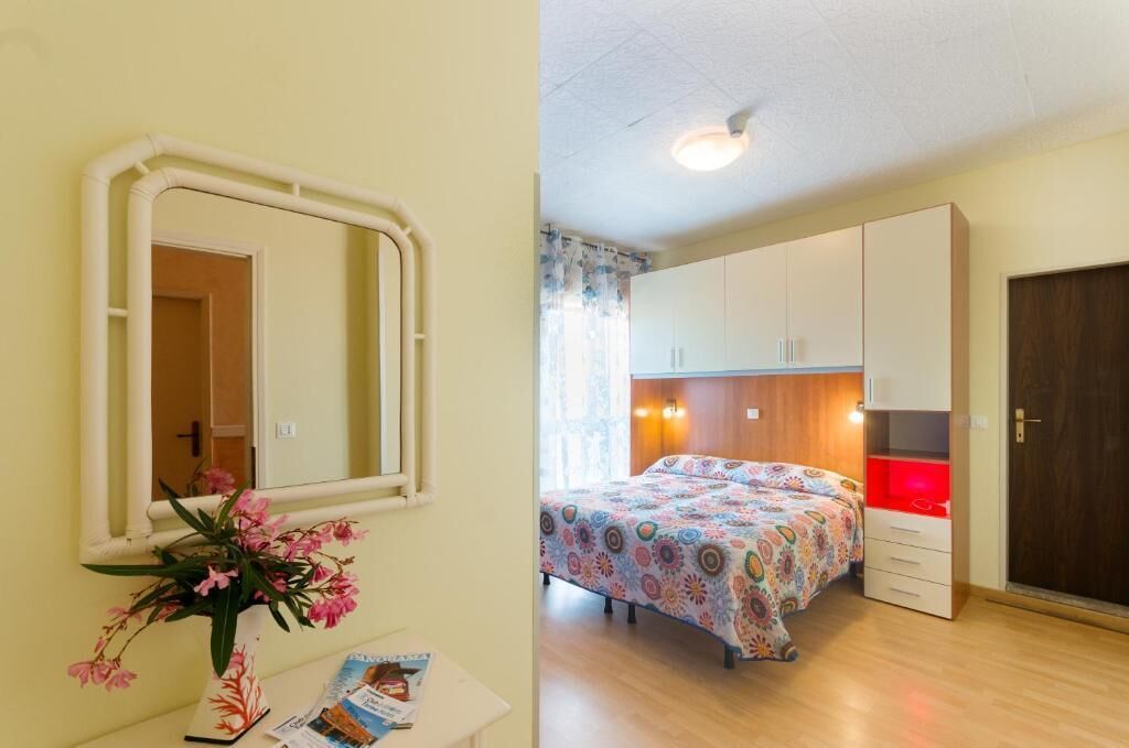 A bedroom with a bed, a dresser, a mirror, and a window with curtains.
