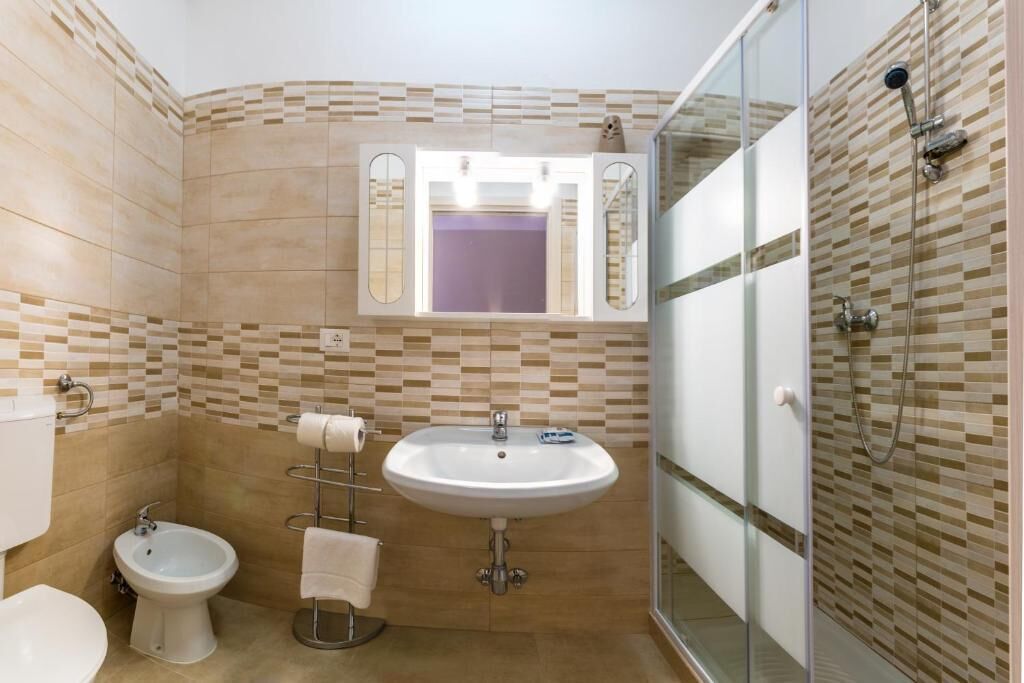 A bathroom with a white sink, a bidet, a glass-enclosed shower, and a mirror above the sink.