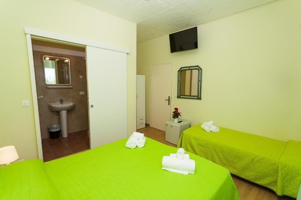Una habitación de hotel con dos camas, un lavamanos, un espejo y un televisor.