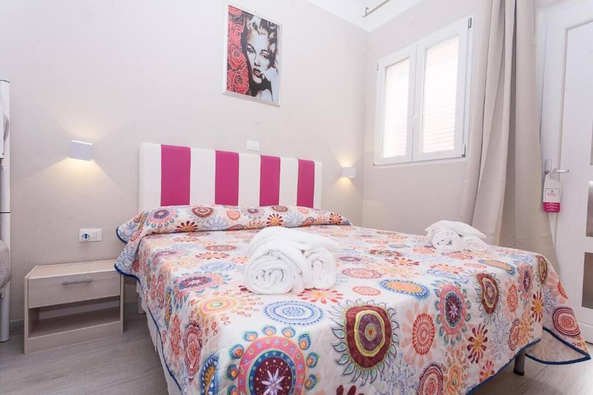 Une chambre à coucher avec un lit, une table de chevet, une lampe fixée au mur, une fenêtre avec des rideaux et une affiche accrochée au mur.