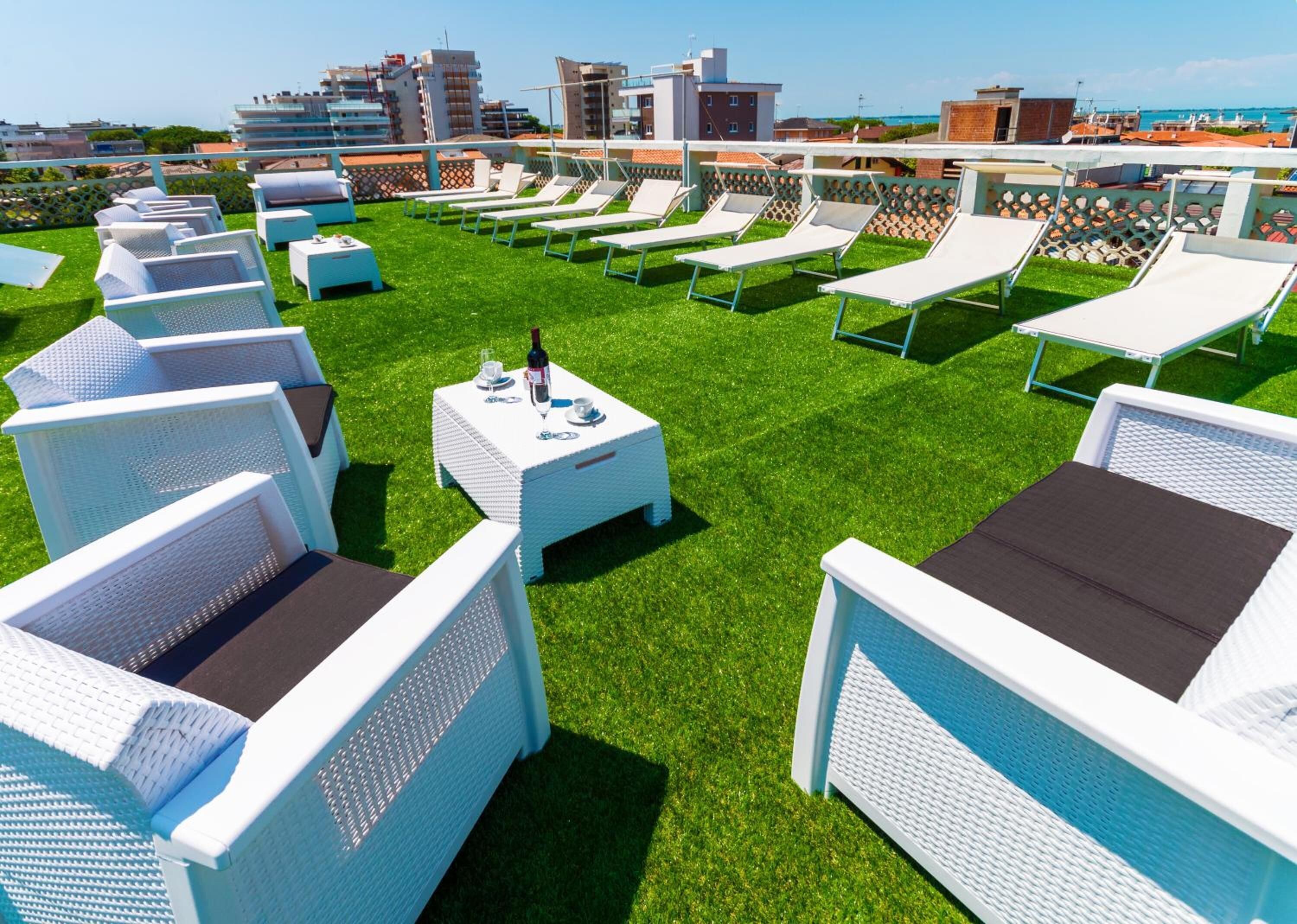 Uma área de lounge no terraço com cadeiras e mesas de vime branco, dispostas sobre um gramado artificial verde.