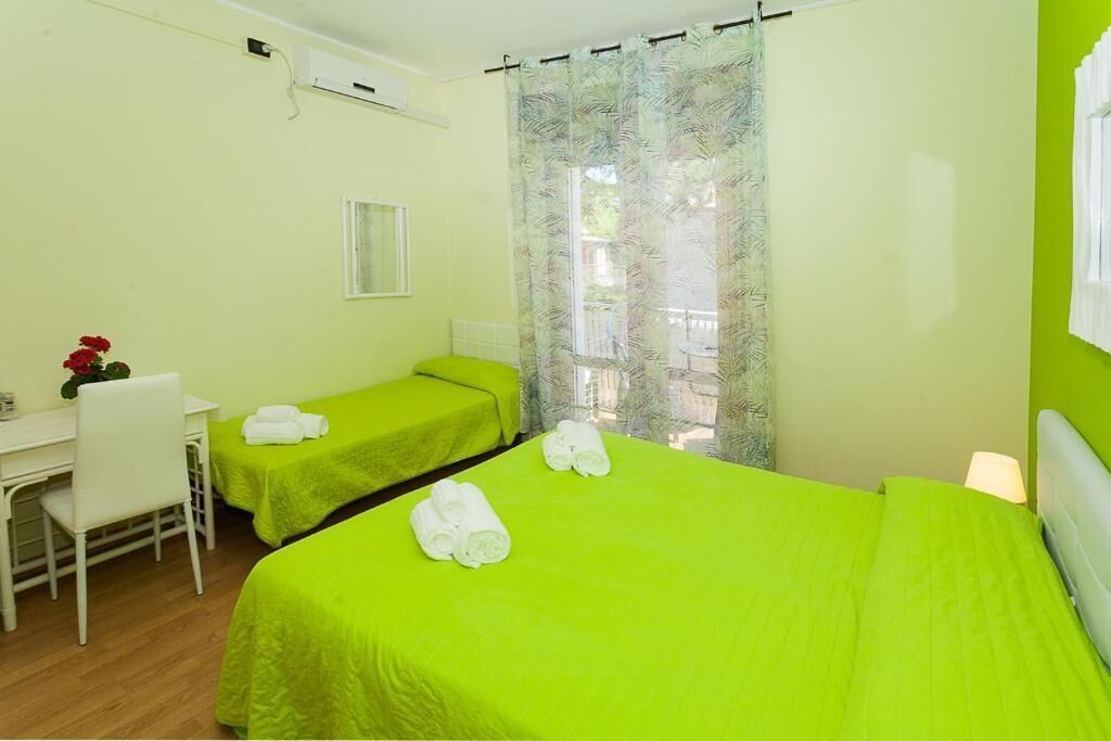 A room with two beds, a desk, a chair, and a window with curtains.