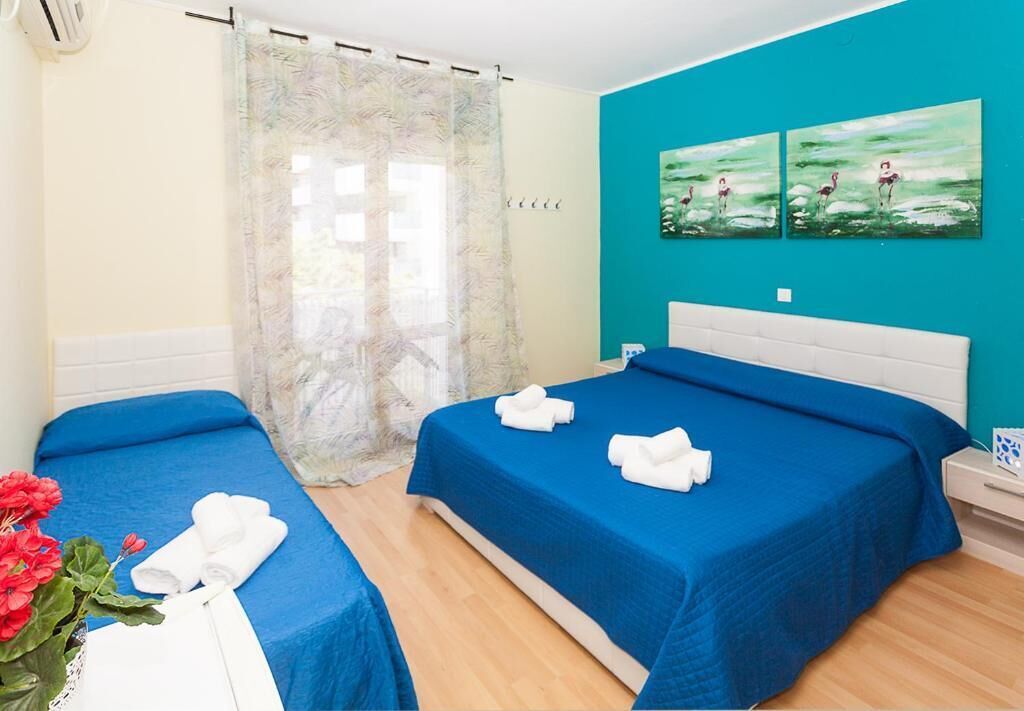 A hotel room with two beds, teal walls, and artwork depicting flamingos.