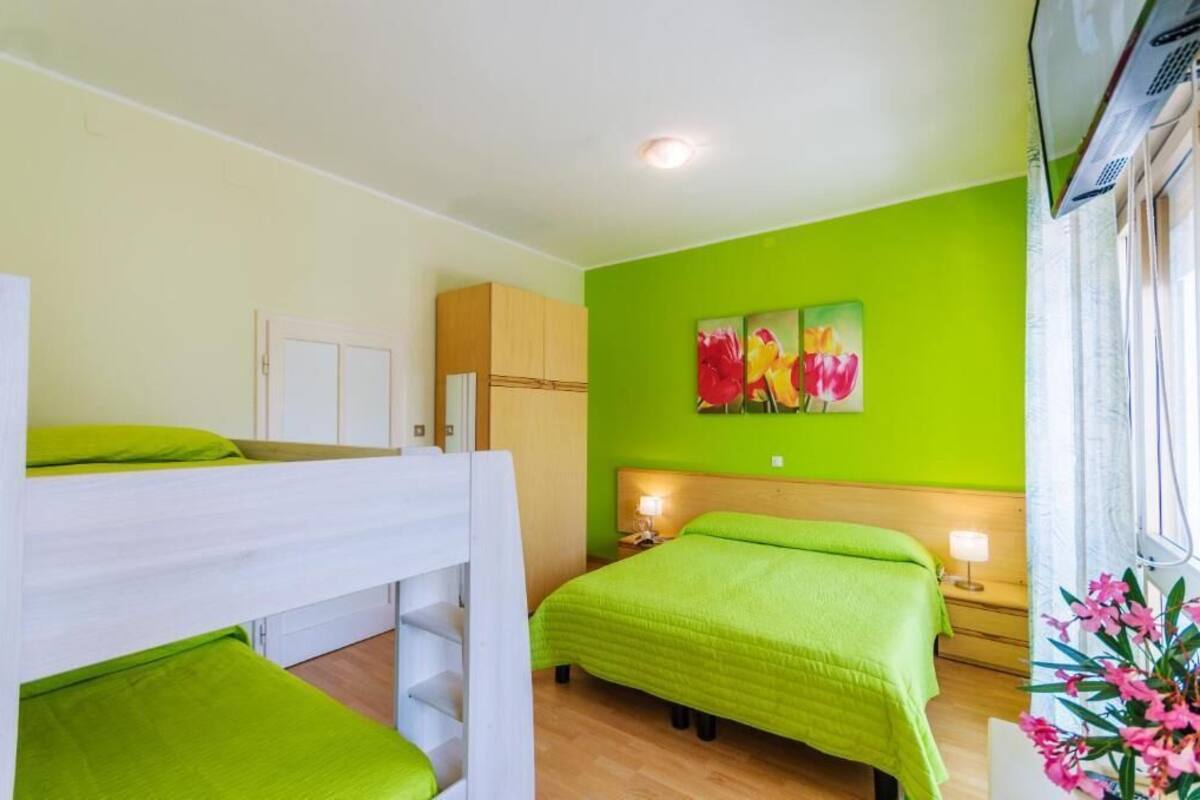 Une chambre avec des lits superposés, un lit, une table de chevet, une lampe et un mur orné d’un tableau représentant des motifs floraux.