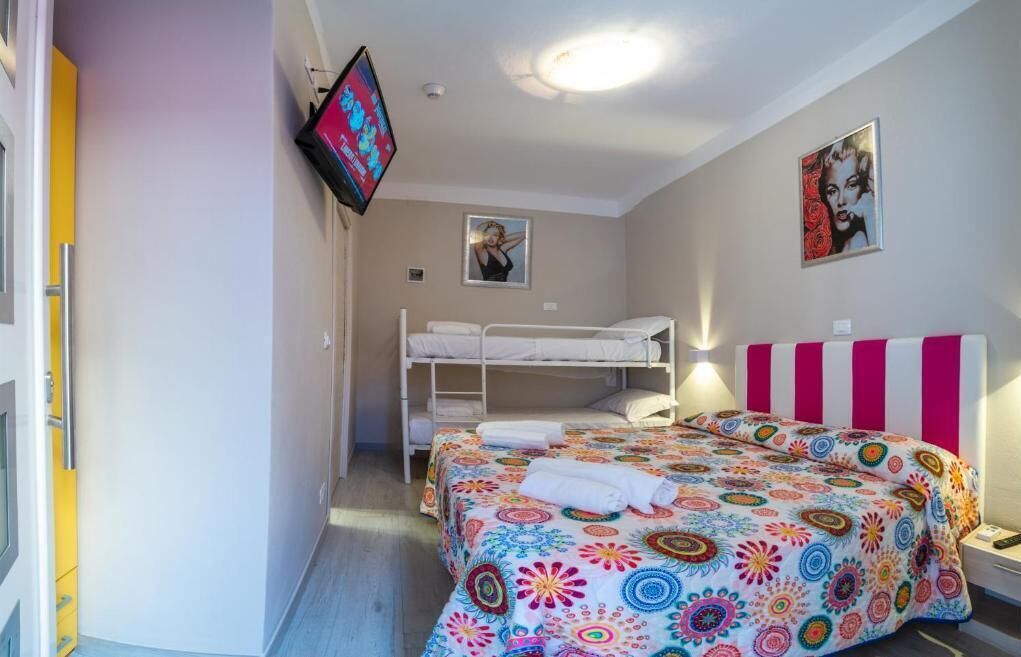 A bedroom with a bunk bed, a colorful bedspread, a TV mounted on the wall, and two posters on the wall.