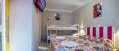 A bedroom with a bunk bed, a colorful bedspread, a TV mounted on the wall, and two posters on the wall.