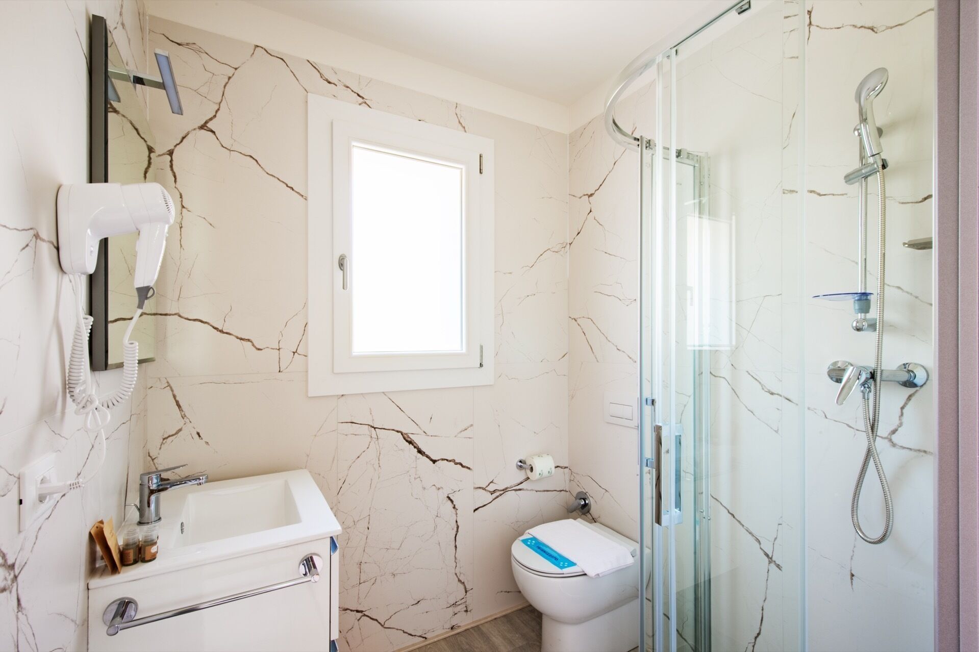 Une salle de bain avec un mur en marbre, un lavabo blanc, des toilettes et une douche à parois de verre.
