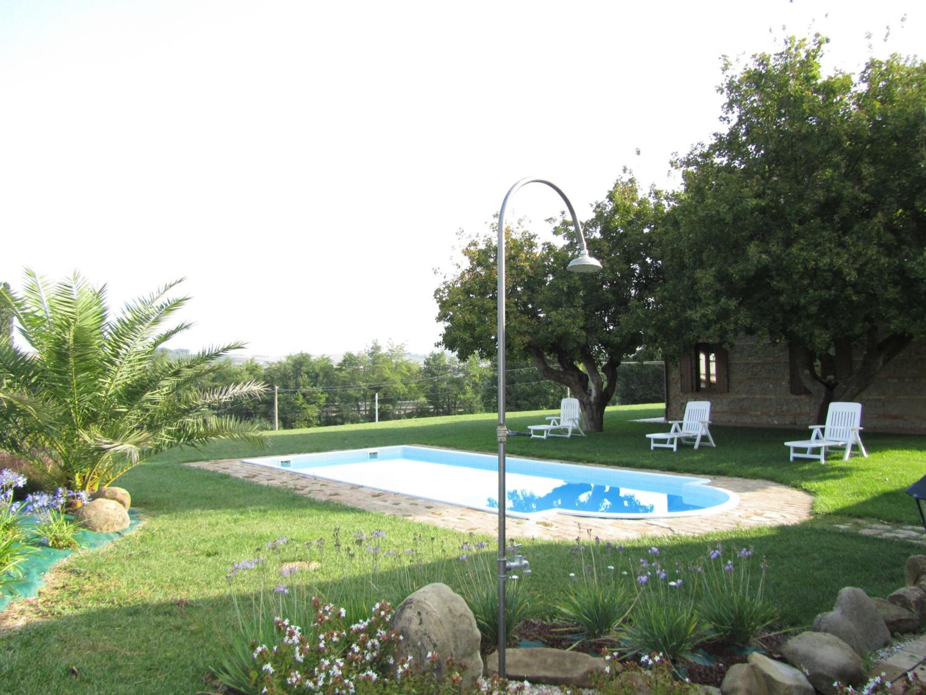 Un patio trasero con piscina, sillas de descanso blancas y un farol.