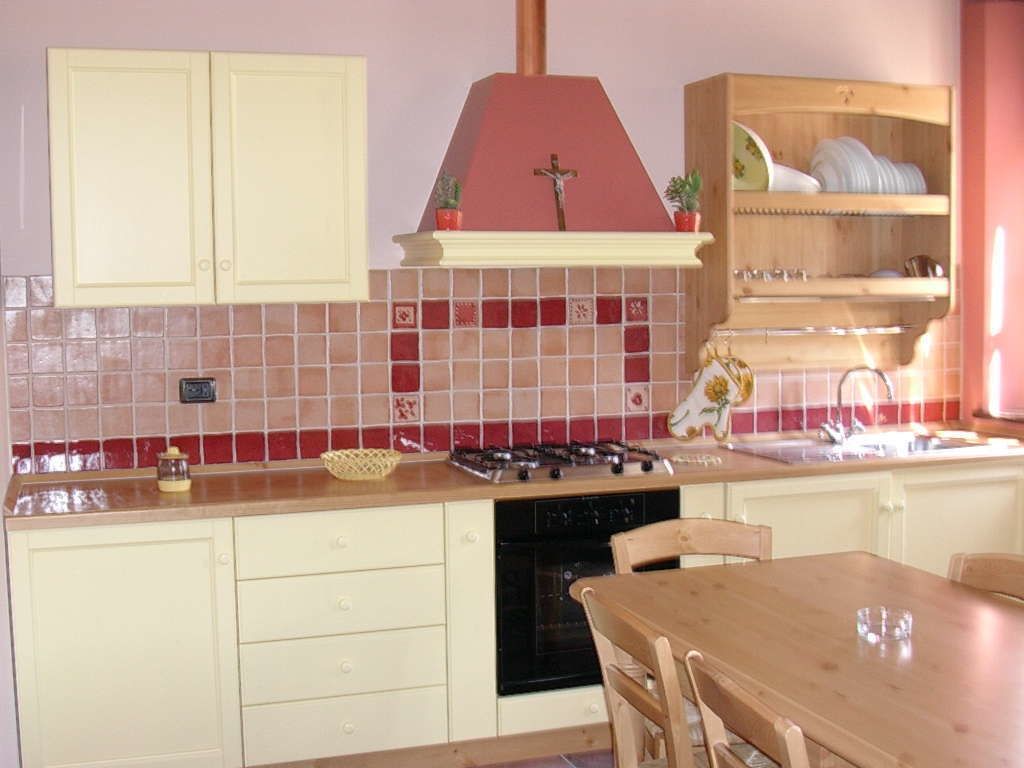 A kitchen with a gas stove, a dishwasher, and a sink. There is a wooden table and chairs, and a shelf with dishes.