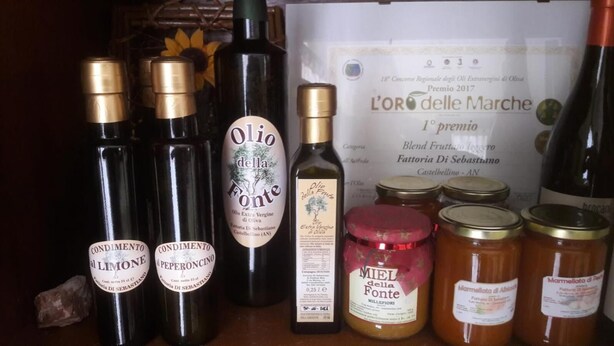Een verzameling olijfoliën en potten, waaronder merken zoals Condimento al Limone en Olio della Fonte, met op de achtergrond een certificaat en andere olijfoliën.