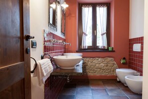 A bathroom with a stone accent wall, a large sink, a toilet, and a window with curtains. - Agriturismo La Vecchia Fonte (Castelbellino)