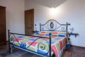 A bed with a metal frame, a colorful quilt, a wooden door, and a wall-mounted light fixture. - Agriturismo La Vecchia Fonte (Castelbellino)
