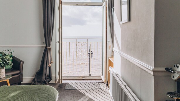 Une pièce avec vue sur la mer, une lampe en osier, une chaise, une petite table avec une plante et un radiateur.