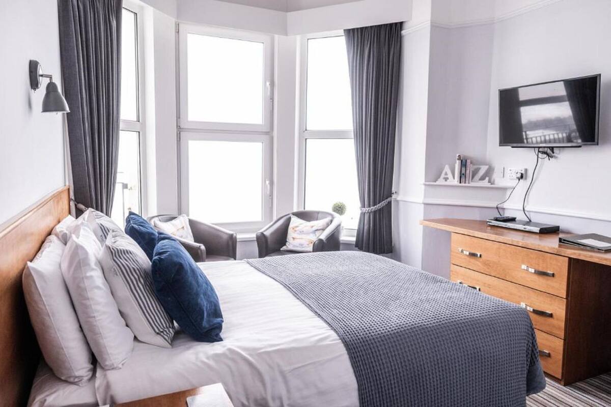 A modern hotel room with a large bed, a desk, a chair, and a TV.