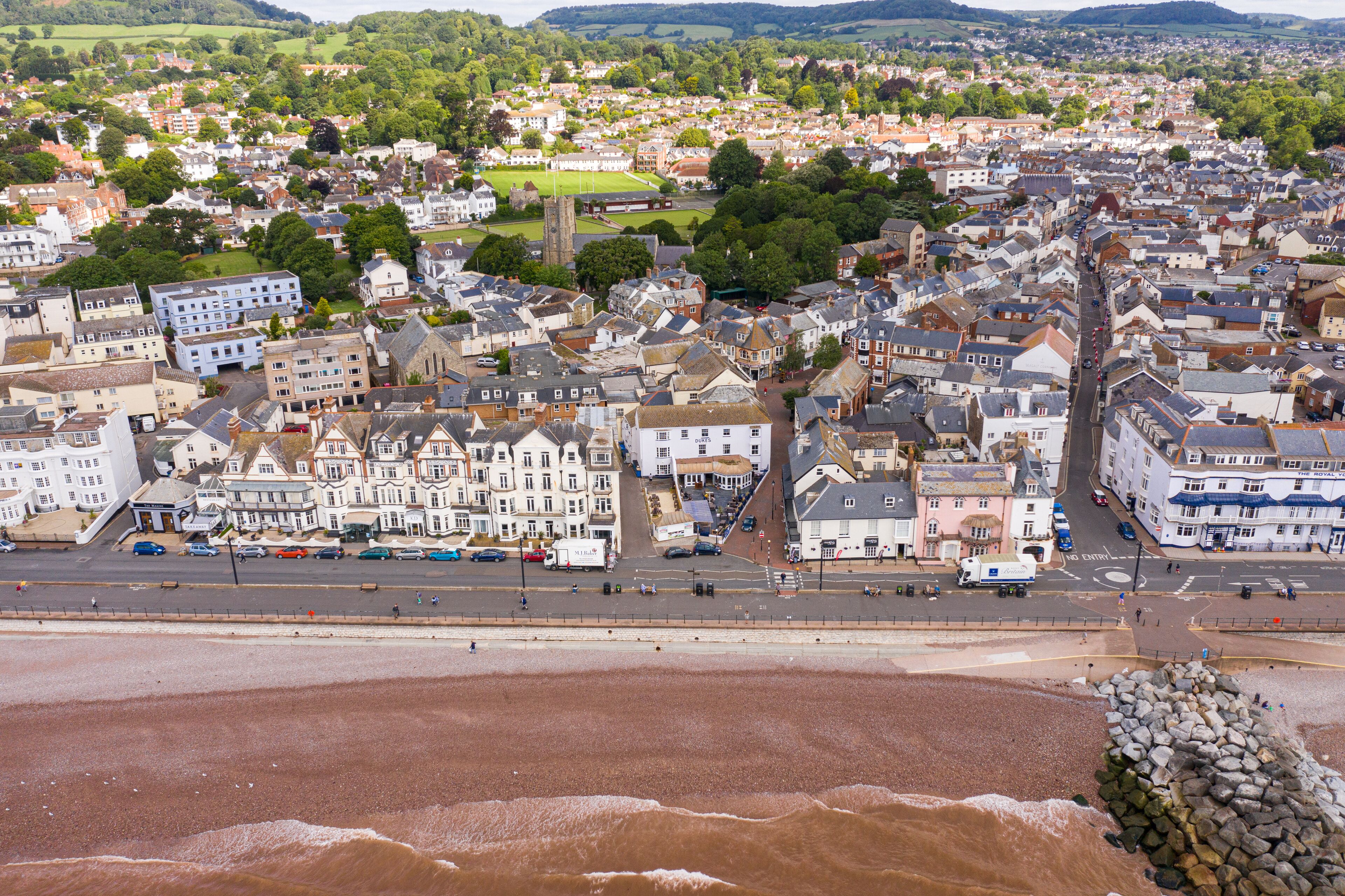 A coastal town with a mix of residential and commercial buildings, a prominent road, and a beach with a rocky breakwater.