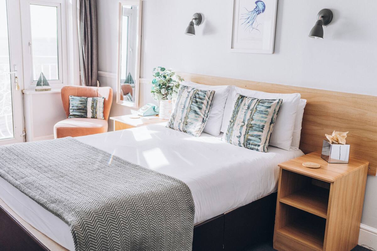 A neatly arranged hotel room with a large bed, a bedside table, a nightstand, a chair, and a window with curtains.