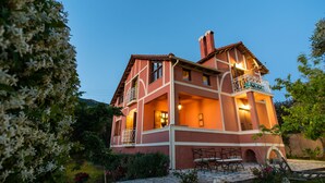 A two-story house with a balcony, a chimney, and a garden with flowers and plants. - Villa Meliti (Corfu)