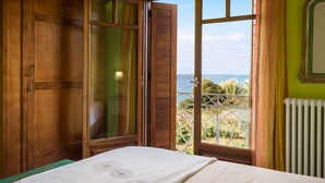 A bedroom with a bed, a wooden wardrobe, and a window with a view of the sea. - Villa Meliti (Corfu)