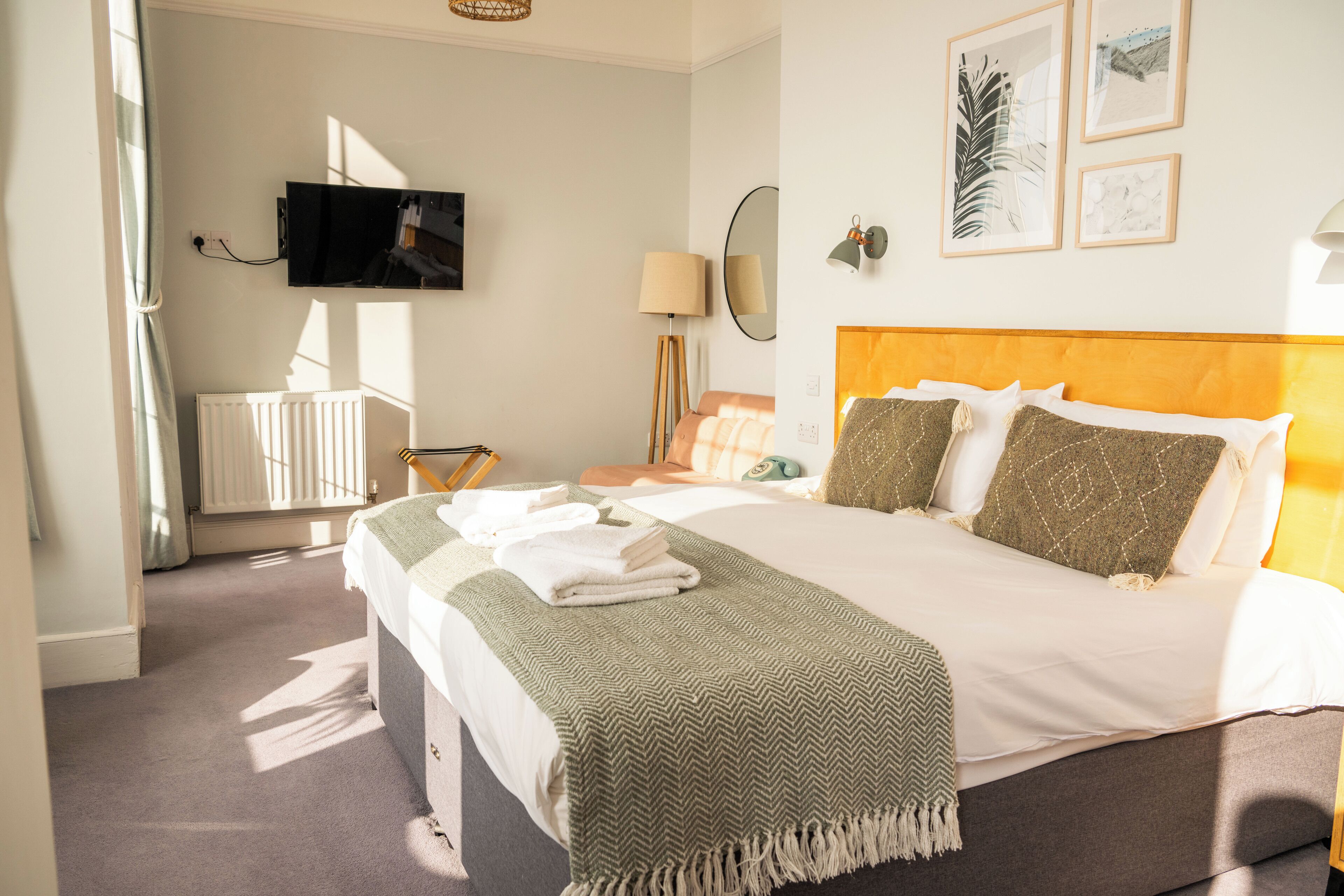 A hotel room with a bed, a television mounted on the wall, a radiator, a lamp, and framed artwork on the wall.