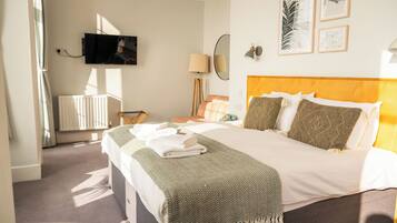 A hotel room with a bed, a television mounted on the wall, a radiator, a lamp, and framed artwork on the wall.