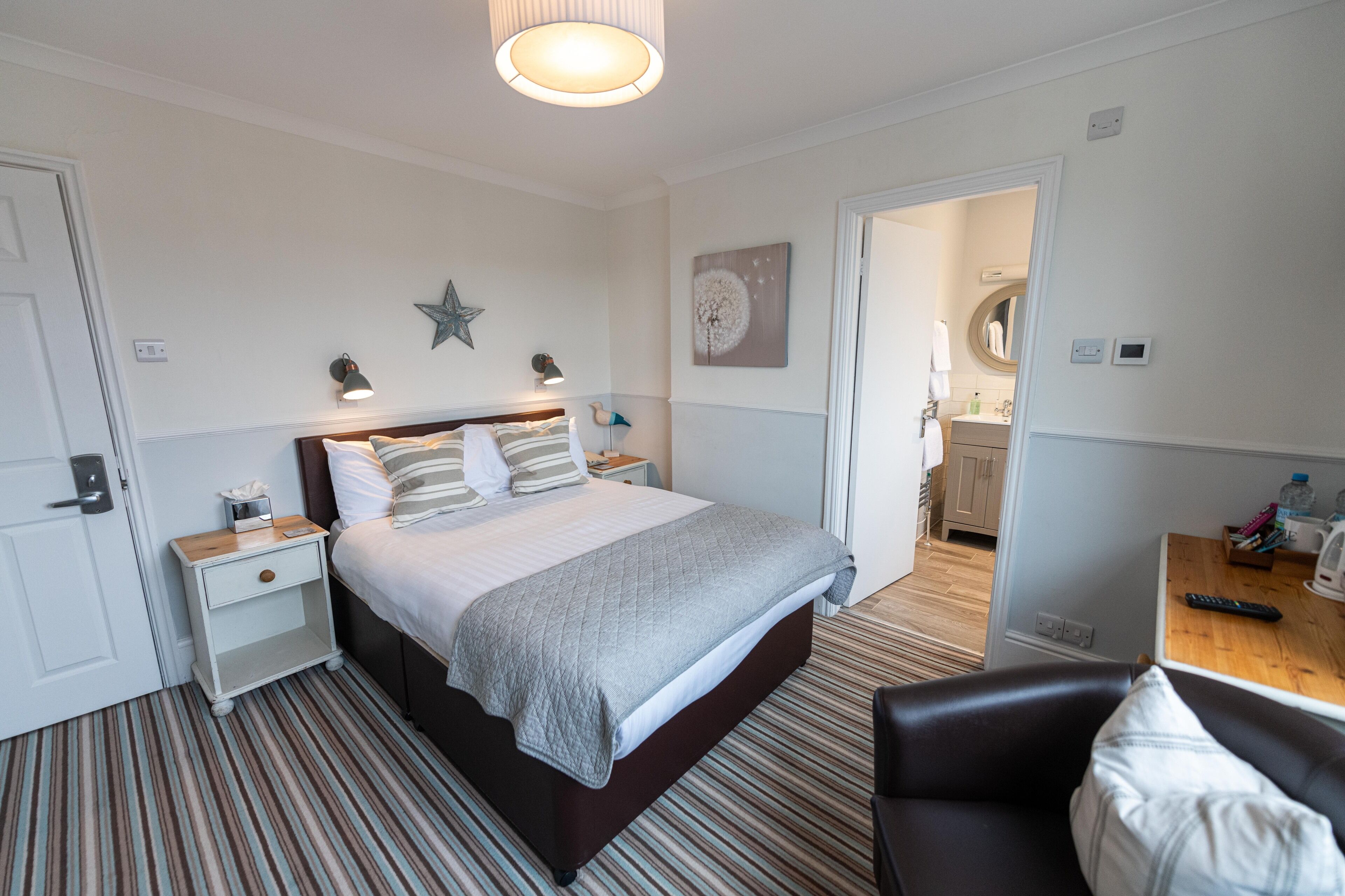 A hotel room with a bed, bedside tables, a desk, a chair, and a bathroom visible through an open door.