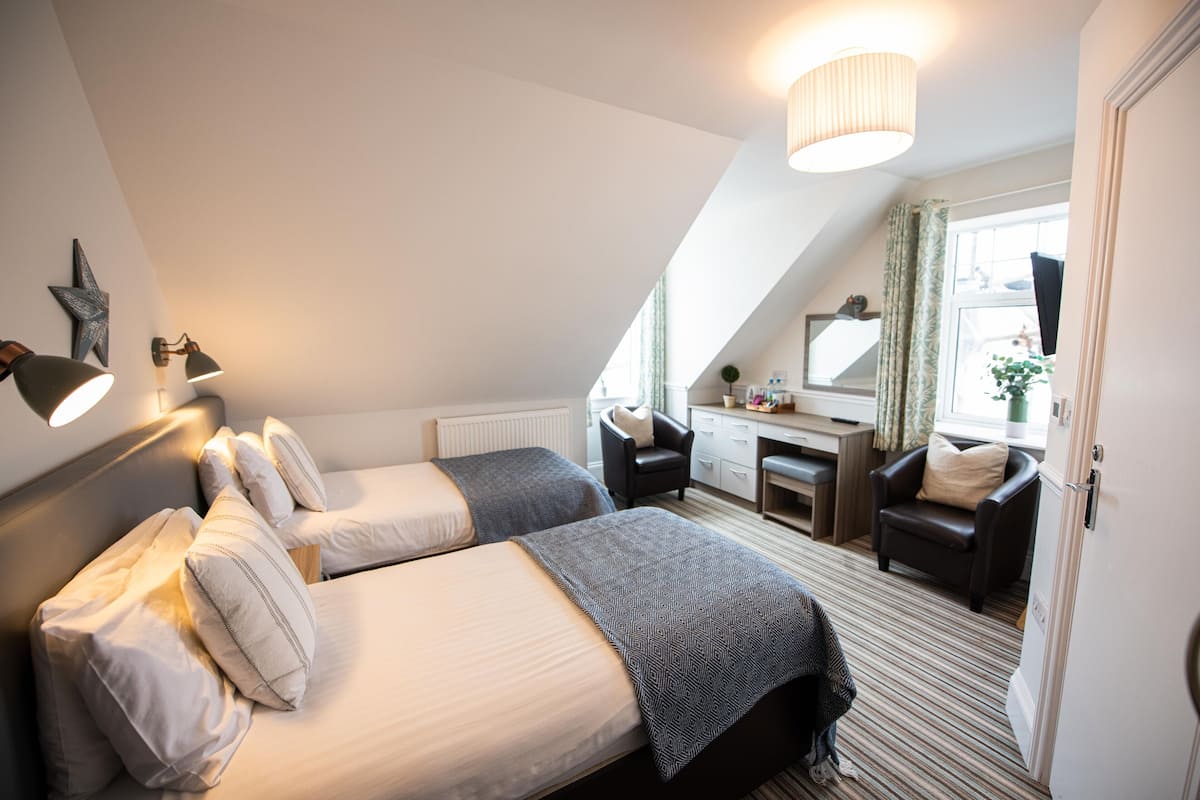 Een slaapkamer met twee bedden, een bureau, een stoel en een groot raam.