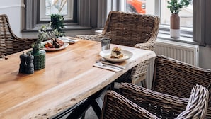 A dining area with a wooden table, wicker chairs, and a large window with curtains.