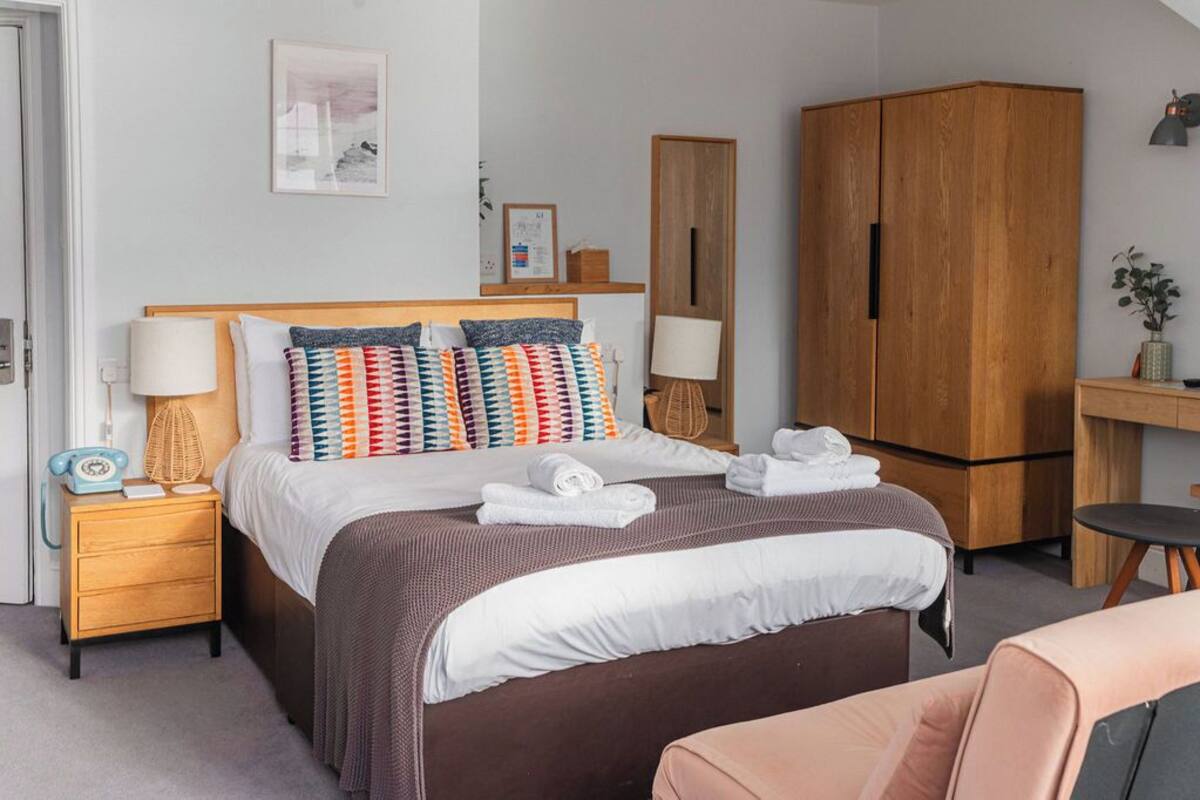 Een keurig opgemaakt slaapkamer met een groot bed, nachtkastjes, een kledingkast en een bureau met stoel.