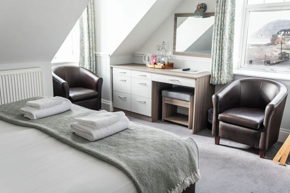 Een slaapkamer met een bed, twee stoelen, een bureau en een raam met uitzicht.