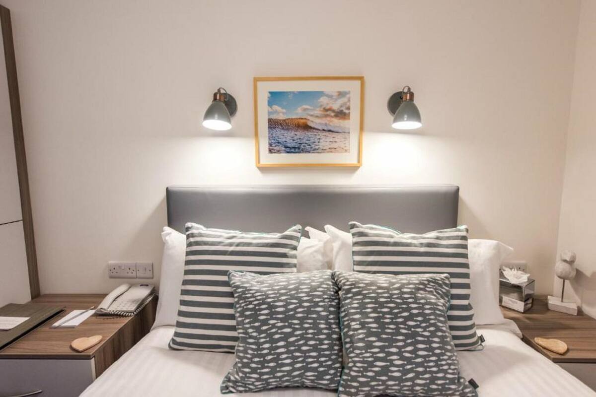 Een netjes opgemaakt bed met gestreepte en patroon kussens, een bedtelefoon en een ingelijste foto aan de muur.
