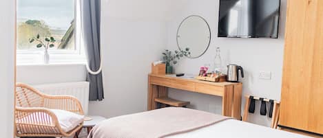 A bedroom with a bed, a desk, a chair, a TV, and a window with a view.