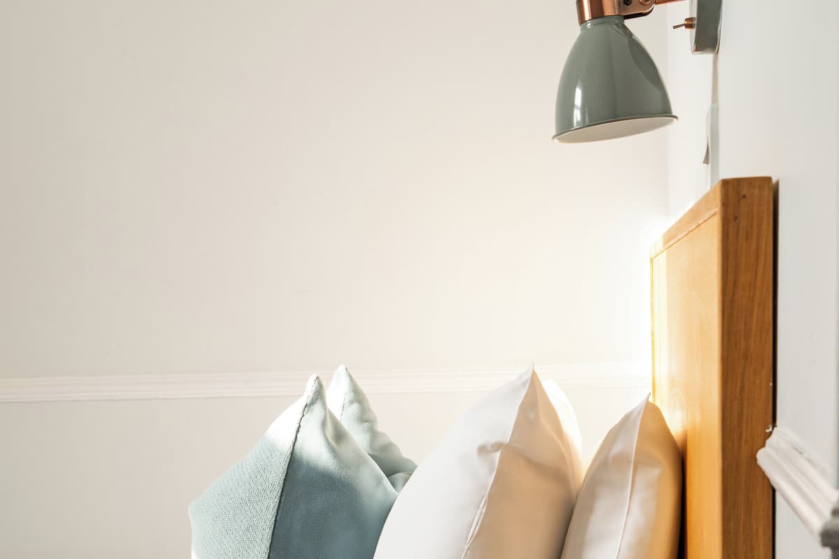 Een netjes opgemaakt bed met kussens, een nachtkastje met een draaischijf telefoon, een lamp en een stuk papier.