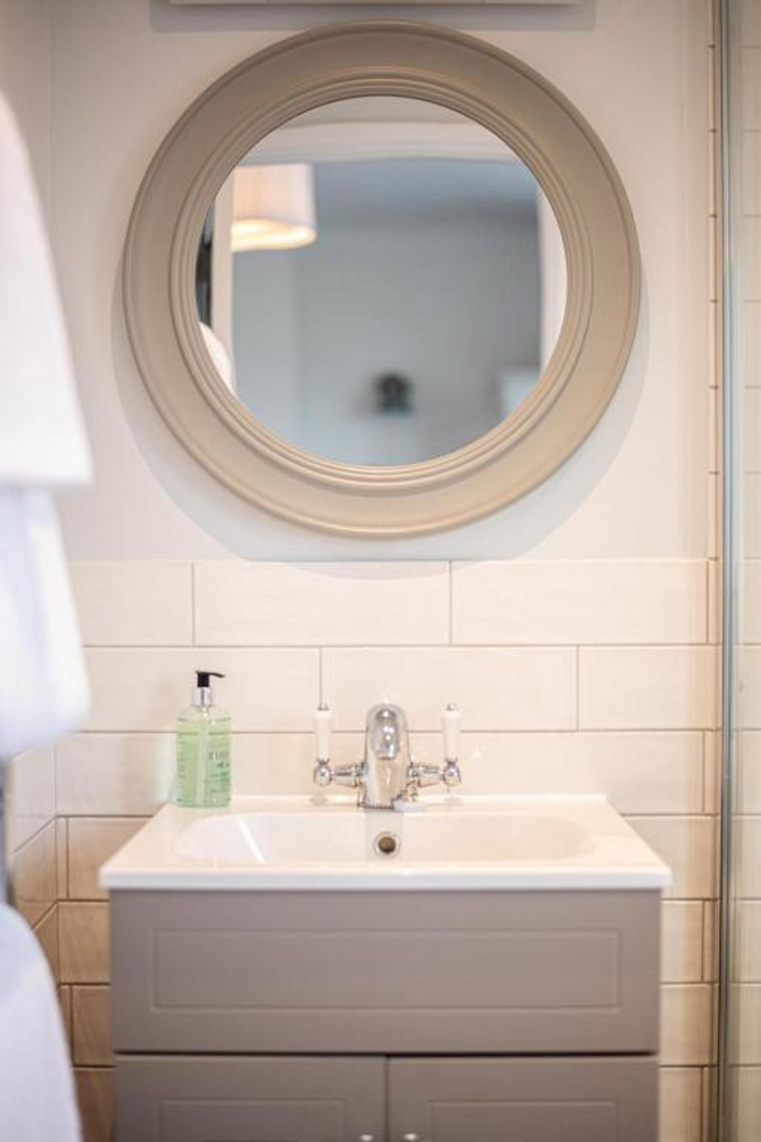 Un baño con un espejo redondo, un lavabo blanco y un mueble gris.