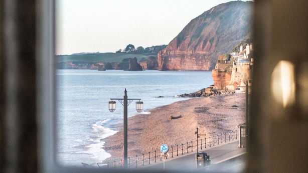A coastal view through a window, featuring a beach, cliffs, and a road with a vehicle.