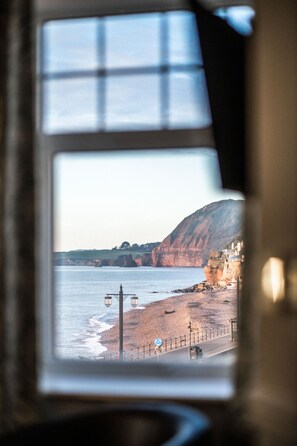 Vista costera a través de una ventana, mostrando una playa, acantilados y una carretera con un vehículo.