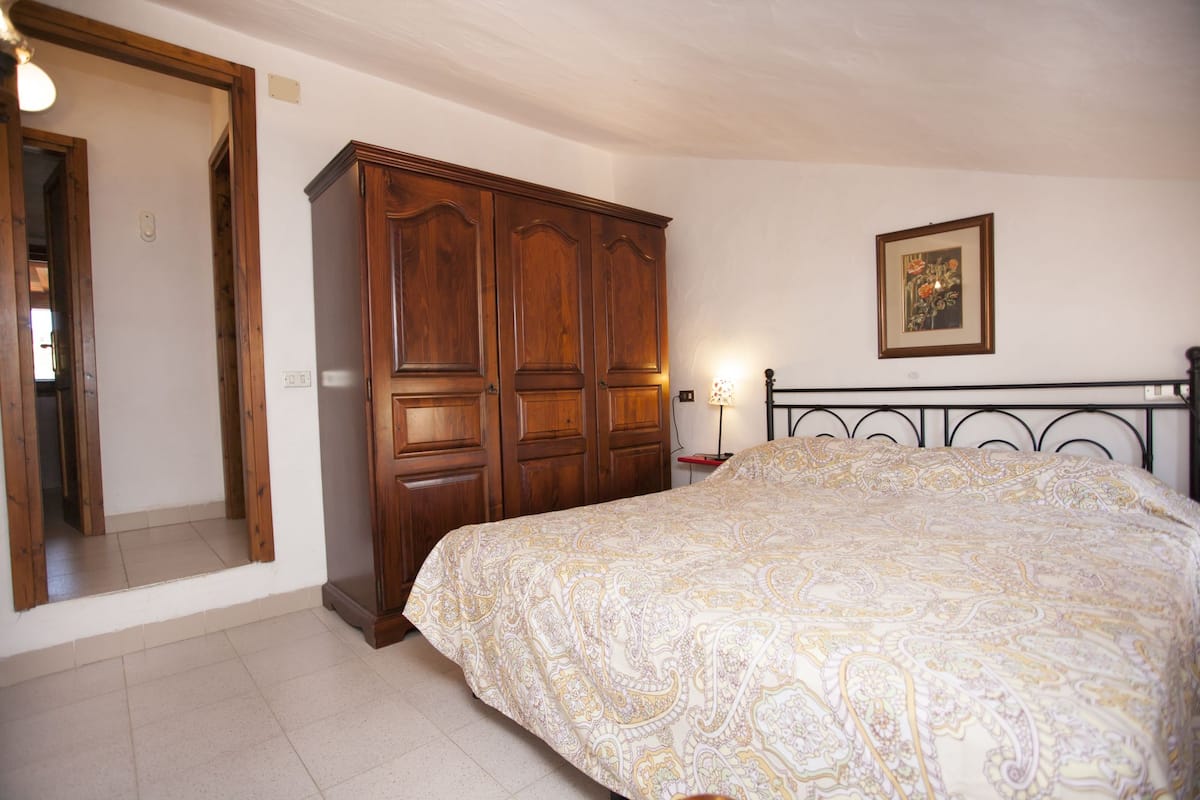 A bedroom with a large bed, wooden wardrobe, and a framed picture on the wall.