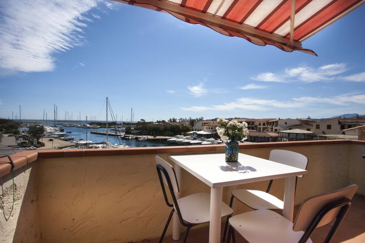 A balcony with a table and chairs, overlooking a marina with boats and buildings.