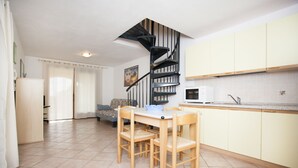 Una cocina moderna con una mesa y sillas de madera, una escalera en espiral negra y armarios de tonos claros.
