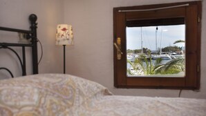 Un dormitorio con cama, mesita de noche, lámpara y ventana con vista al puerto deportivo.