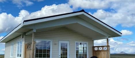 Une maison de plain-pied dotée d’un porche abrité, d’un petit espace extérieur aménagé pour s’asseoir et offrant une vue sur le paysage environnant.